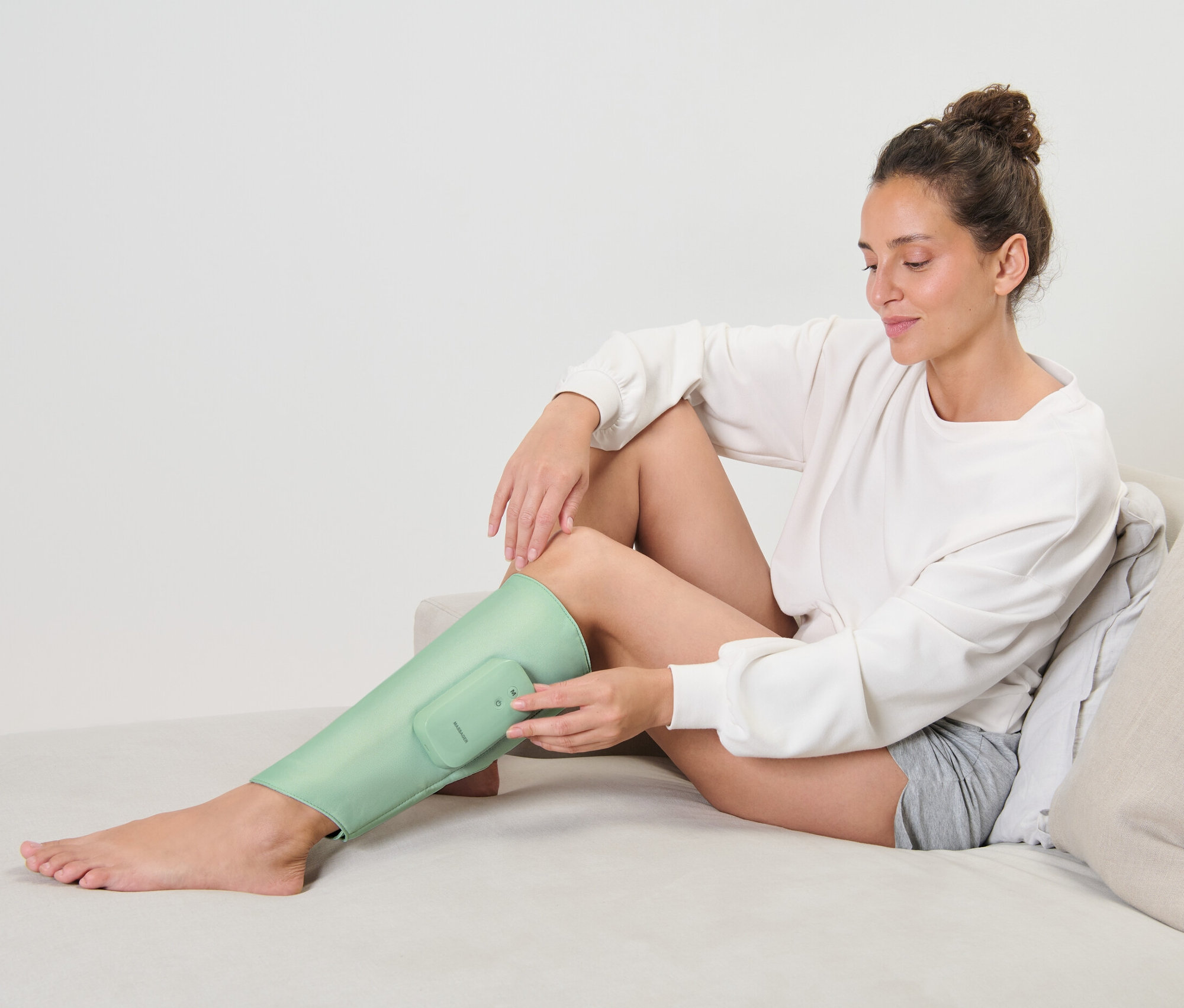 Une femme assise sur un canapé utilise une manchette de massage sans fil sur sa jambe.