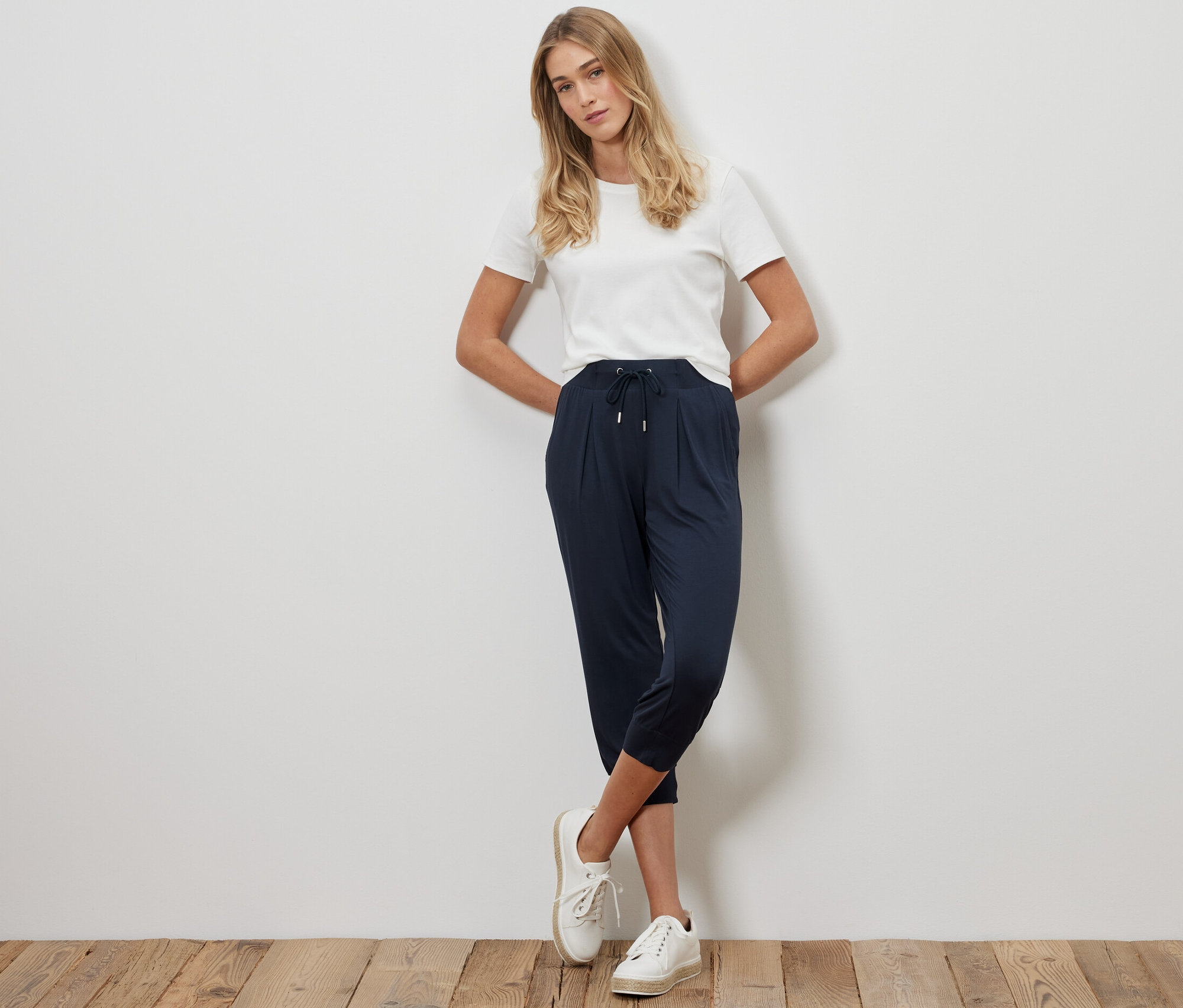 Femme blonde posant en pantalon 3/4 en jersey bleu foncé et t-shirt blanc.