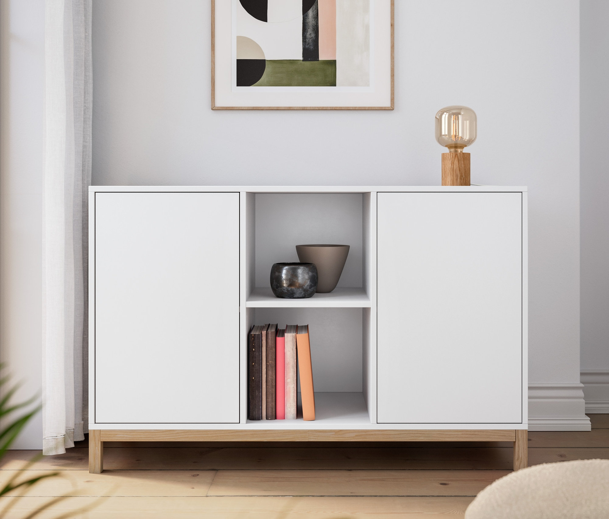 Buffet blanc avec lampe de table en bois. Un tableau est accroché au mur.