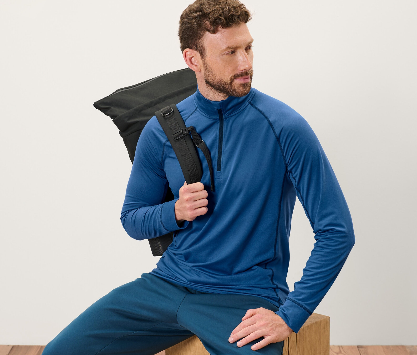 Un homme est assis et porte un t-shirt technique thermique bleu et un sac à dos noir.