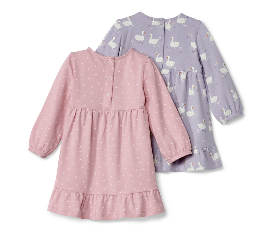 Deux robes en jersey pour bébé : une rose à pois blancs et une violette avec un imprimé de cygnes.