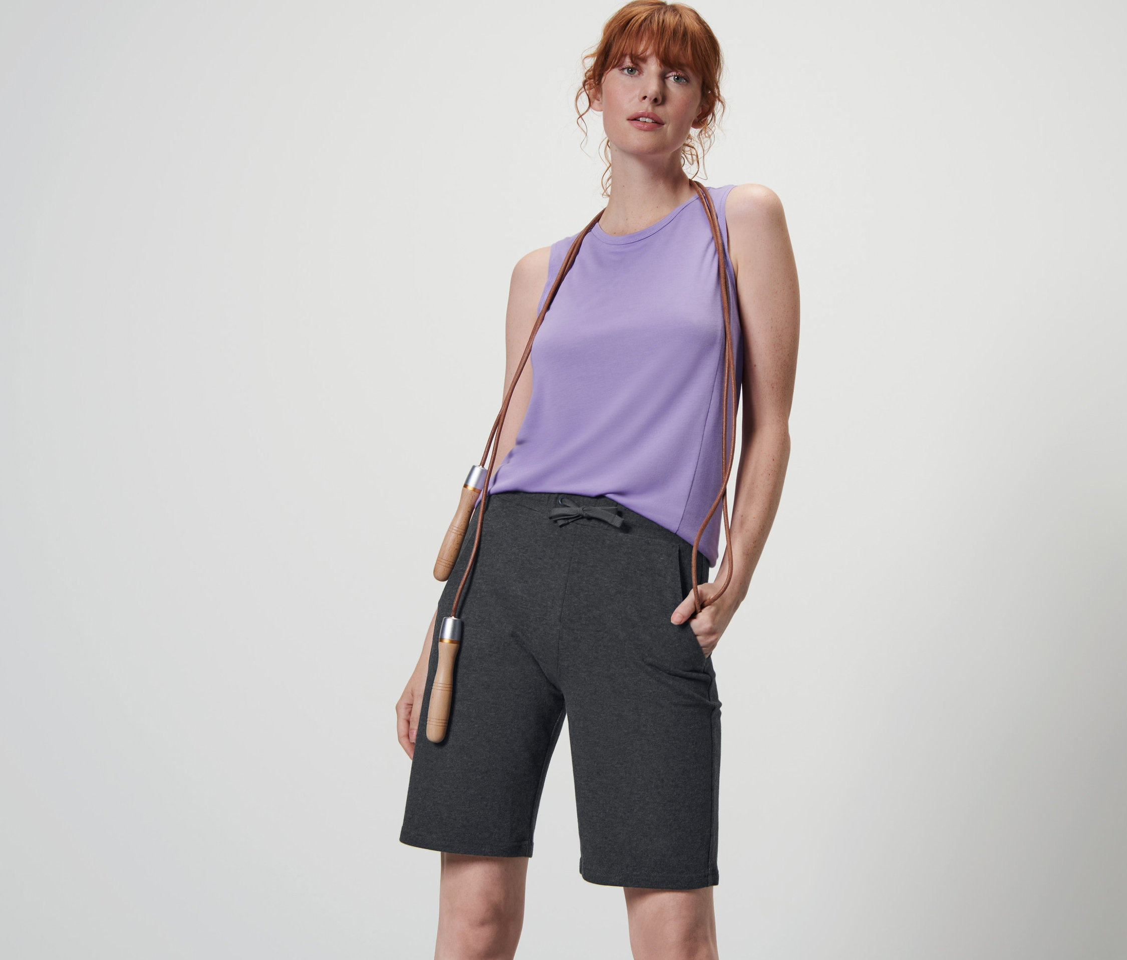 Femme posant en short fonctionnel anthracite et haut violet avec une corde à sauter autour du cou.