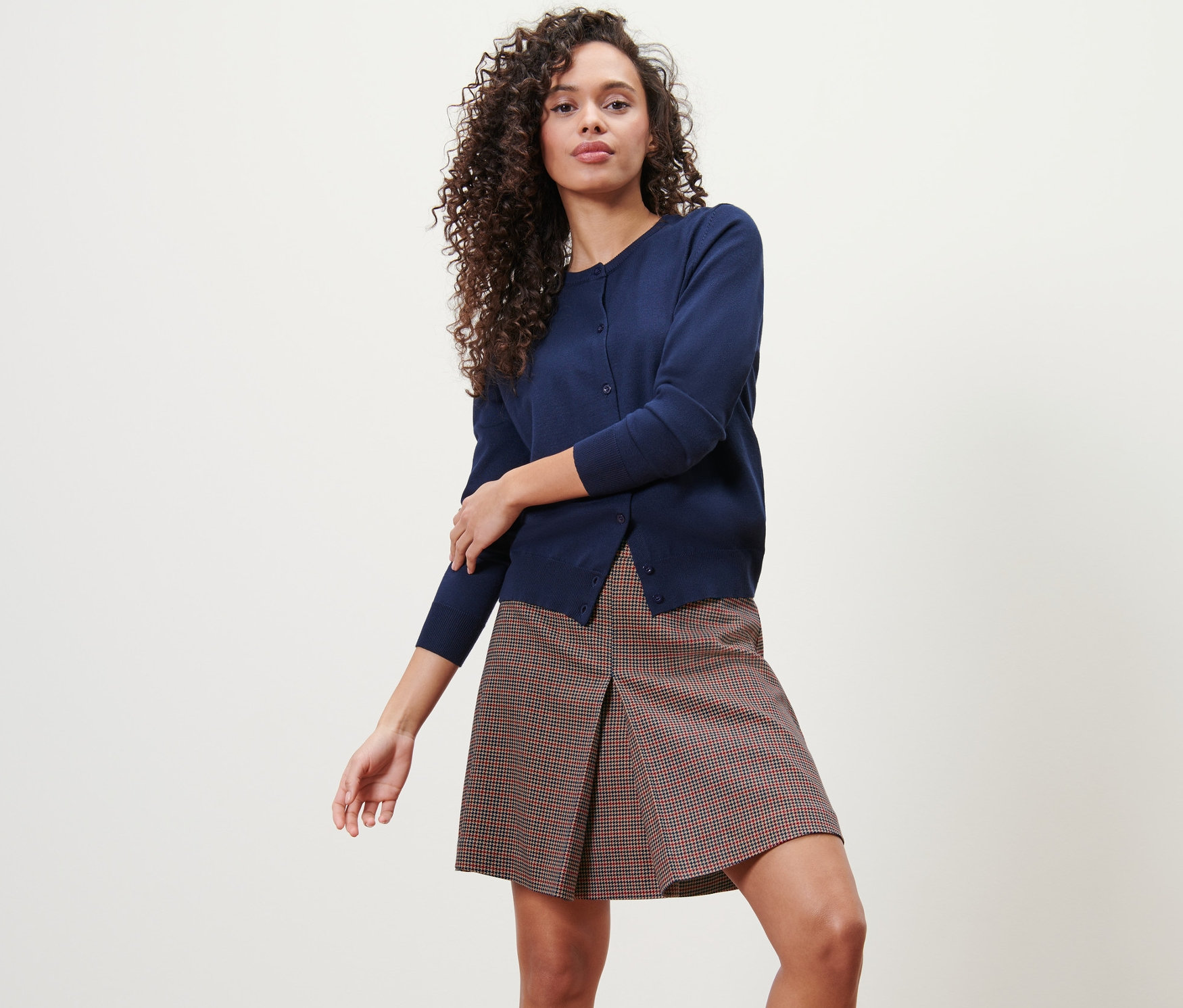 Femme posant en jupe tissée à carreaux et cardigan.