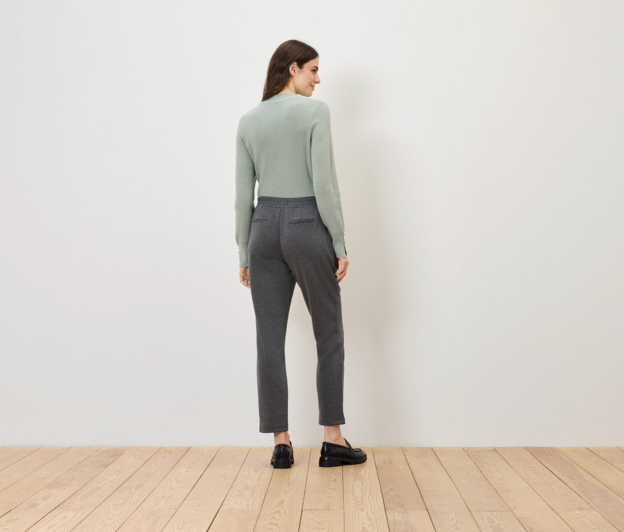 Femme en pull vert clair et pantalon gris, dos au spectateur.