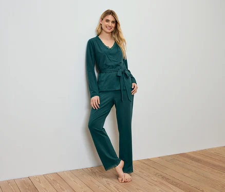 Femme en pyjama vert appuyée contre un mur.