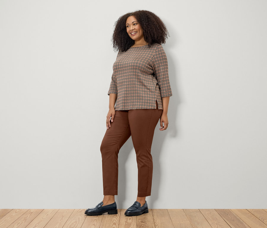 Femme posant en sweat-shirt marron 3/4, pantalon marron et chaussures noires.