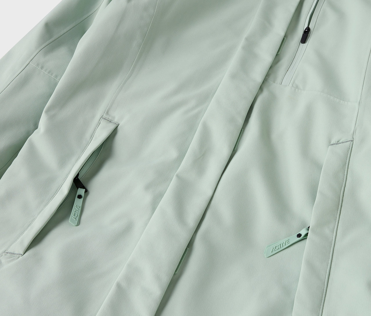 Détail d'une veste vert clair avec des poches zippées.