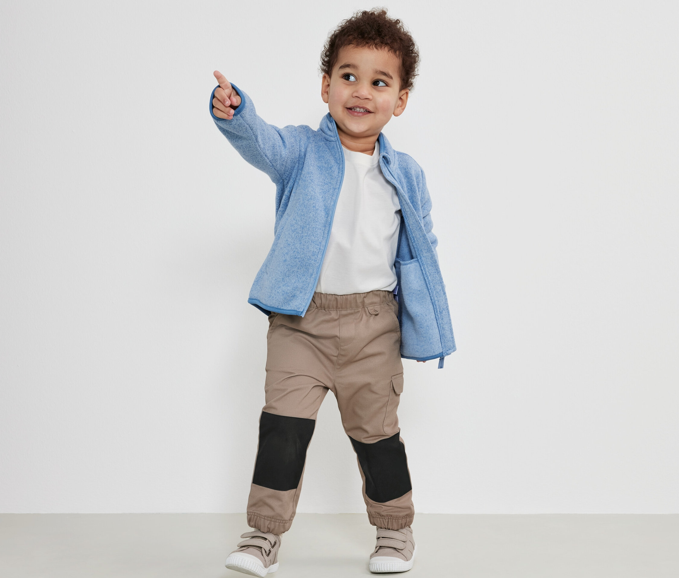 Garçon pointant du doigt, portant un pantalon d’extérieur pour enfant, une veste en polaire bleue et un t-shirt blanc.