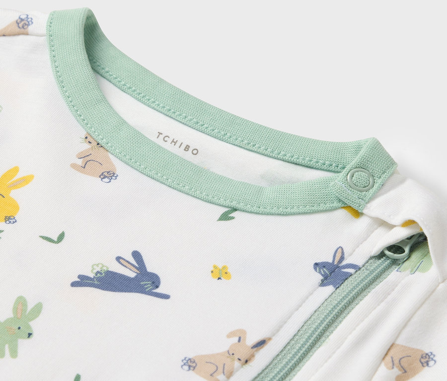 Gros plan sur un pyjama bébé avec motif de lapins et bordure verte.