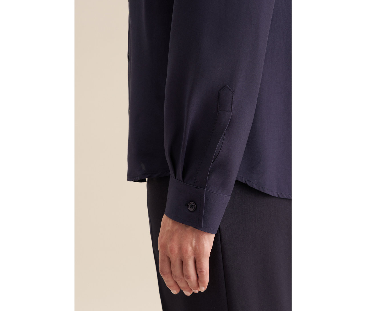 Gros plan sur un bras et une main portant un chemisier en viscose Seidensticker bleu marine avec un poignet boutonné.