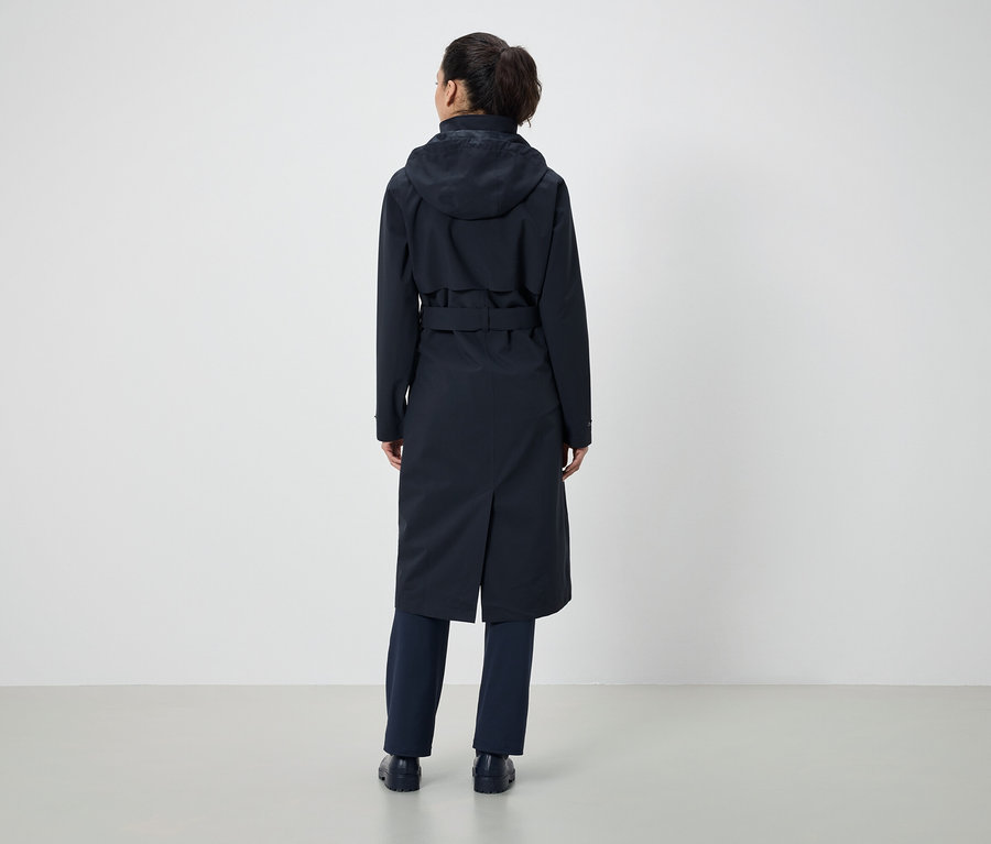 De dos, une femme avec une queue de cheval porte un manteau bleu foncé avec une capuche et une ceinture, ainsi qu'un pantalon bleu foncé.