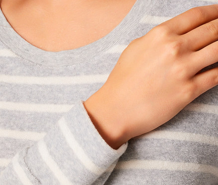 Gros plan sur un pull gris à rayures blanches pour femme avec une main sur la poitrine.