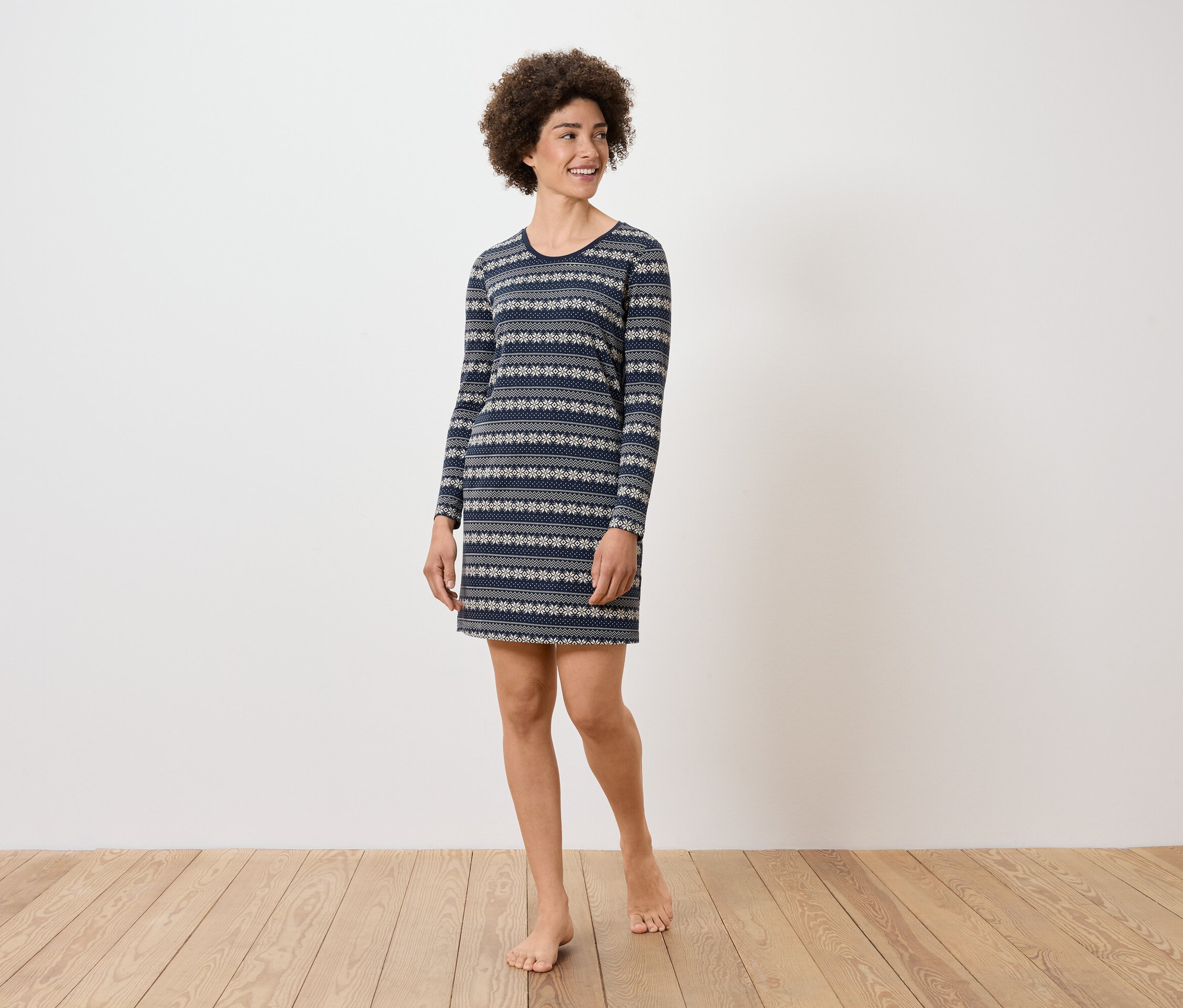 Une femme aux cheveux bouclés porte une robe bleue à manches longues avec un motif.