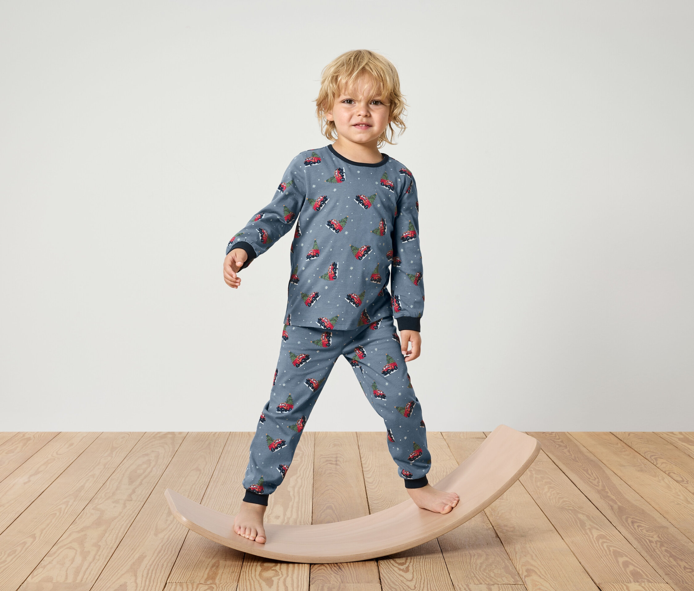 Un garçon en pyjama bleu à imprimé de Noël se tient sur une planche d'équilibre en bois.