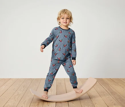 Un garçon en pyjama bleu à imprimé de Noël se tient sur une planche d'équilibre en bois.