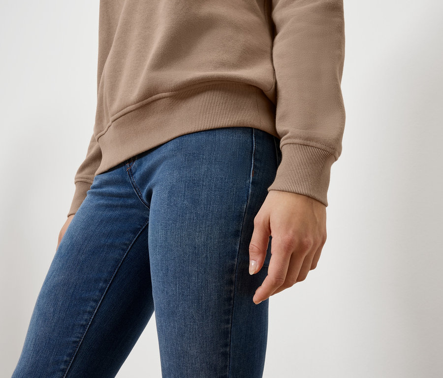 Vue rapprochée d'une femme portant un pull beige et un jean bleu.