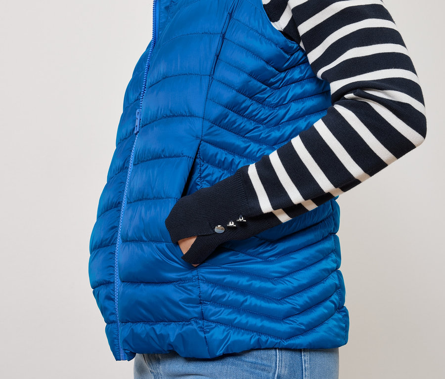 Une personne a sa main dans la poche d'un gilet bleu matelassé et porte un haut rayé bleu marine et blanc.