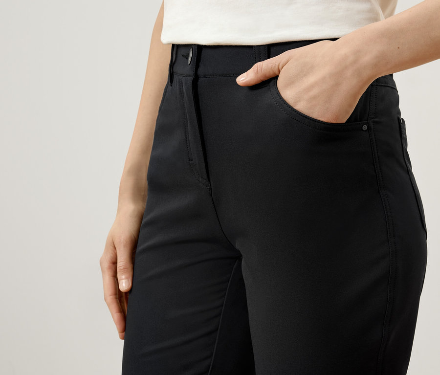 Une femme a la main dans la poche d'un pantalon noir.