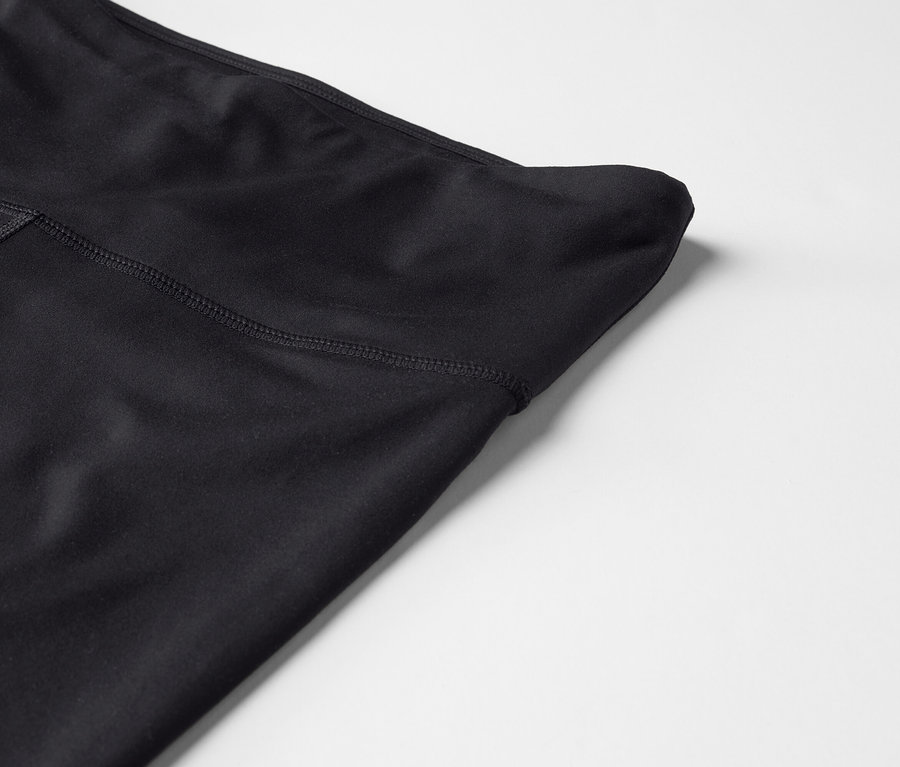 Gros plan d'un legging noir taille haute sur un fond blanc.