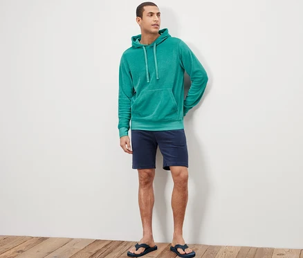 Un homme debout portant un sweatshirt à capuche en tissu éponge, un short et des tongs.