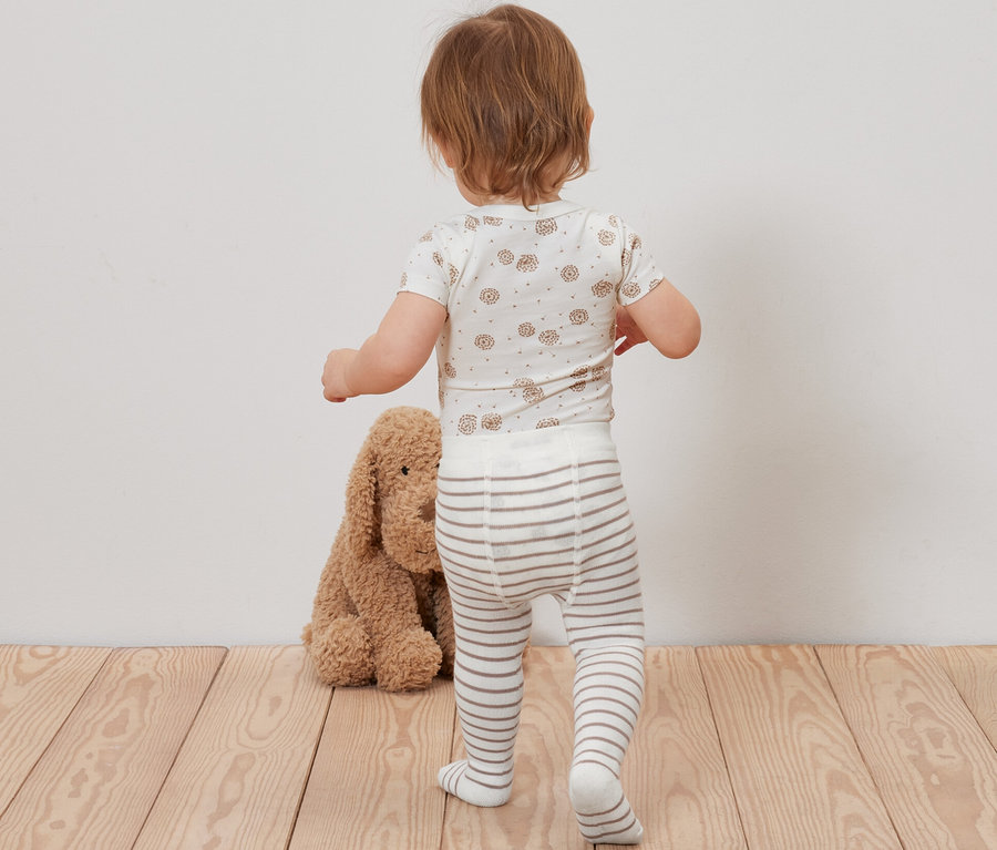 Bébé se tient dos à la caméra et porte 5 paires de bas pour bébé.