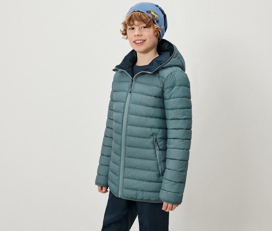 Un garçon porte une veste 2-en-1 Kinder Softshell et Steppjacke et un bonnet bleu.