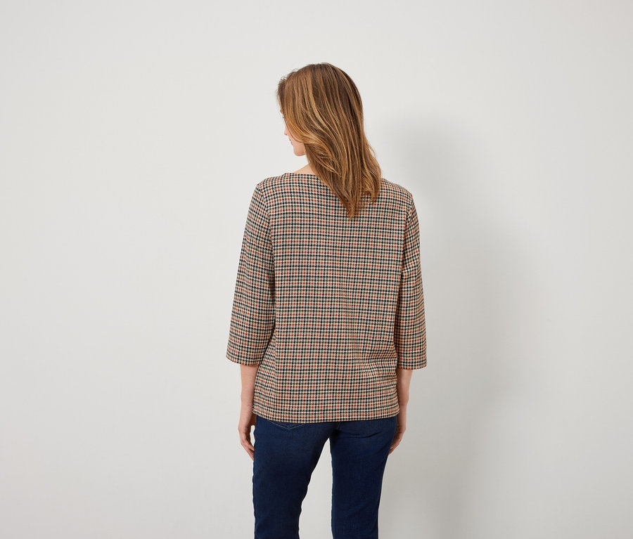 Une femme, dos à la caméra, porte un chemisier à carreaux et un jean.
