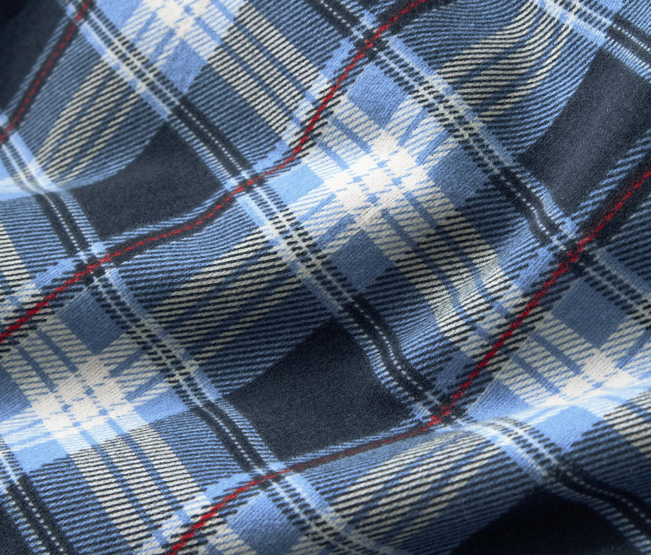 Gros plan sur un tissu à motif écossais bleu, complété par des rayures blanches et rouges fines.