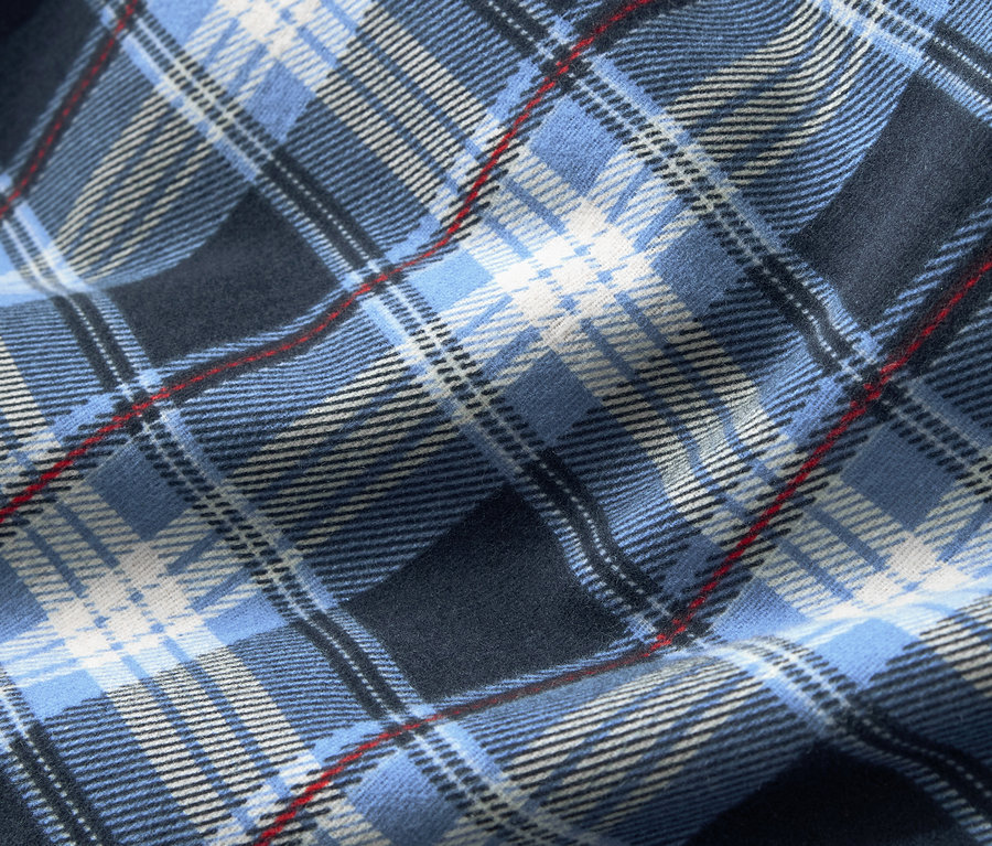 Gros plan sur un tissu à motif écossais bleu, complété par des rayures blanches et rouges fines.