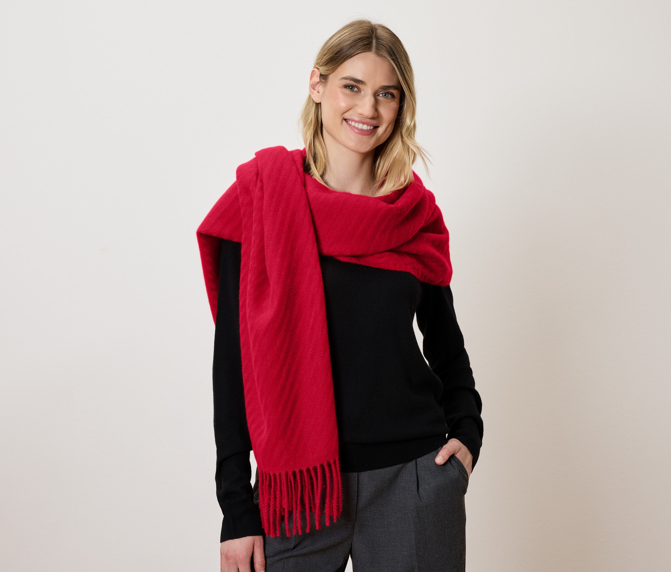 Une femme blonde souriante porte une écharpe rouge et un pull noir.