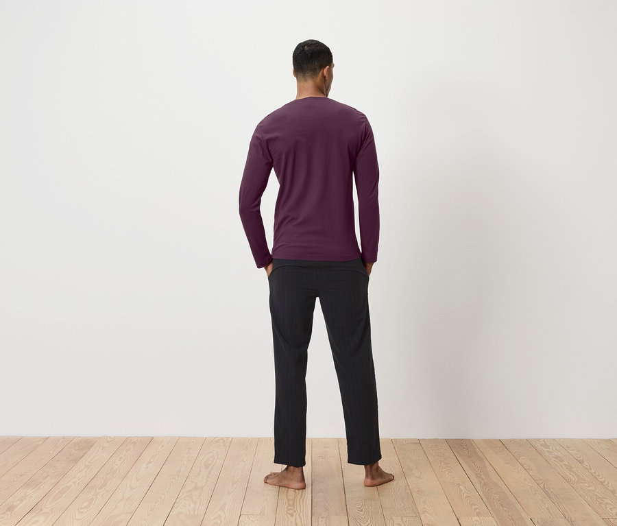 Un homme, vu de dos, porte un t-shirt bordeaux à manches longues et un pantalon noir.