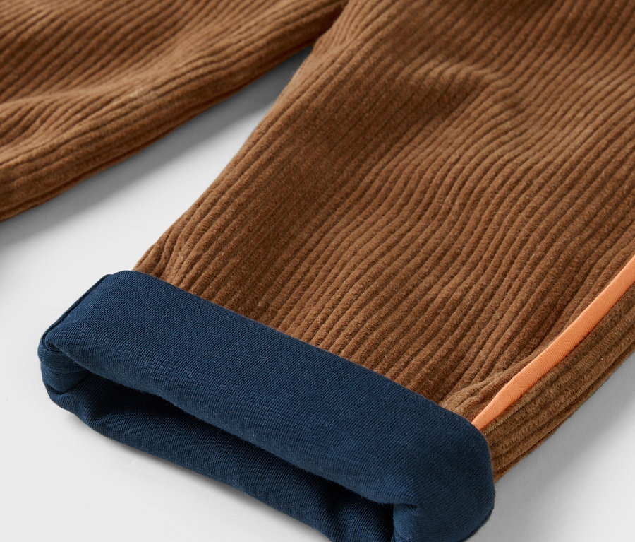 Détail d'un pantalon en velours côtelé marron avec un ourlet bleu foncé au bas de la jambe.