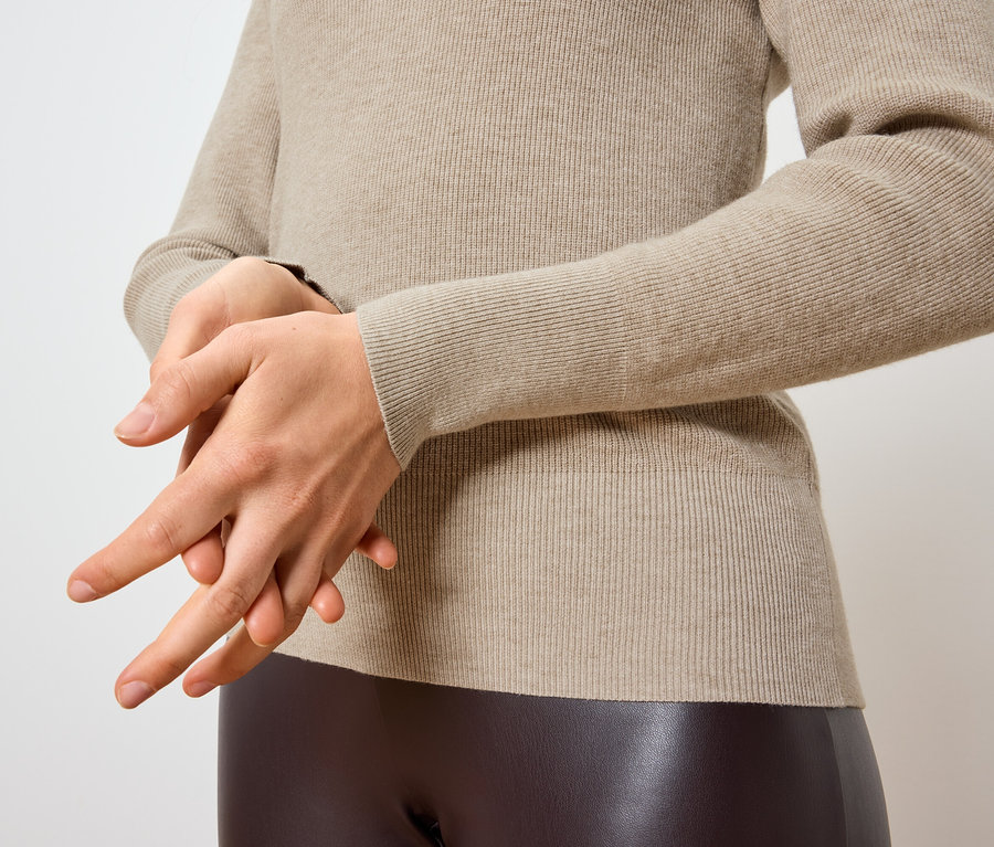 Une femme se frotte les mains sur un pull crème et un legging marron.