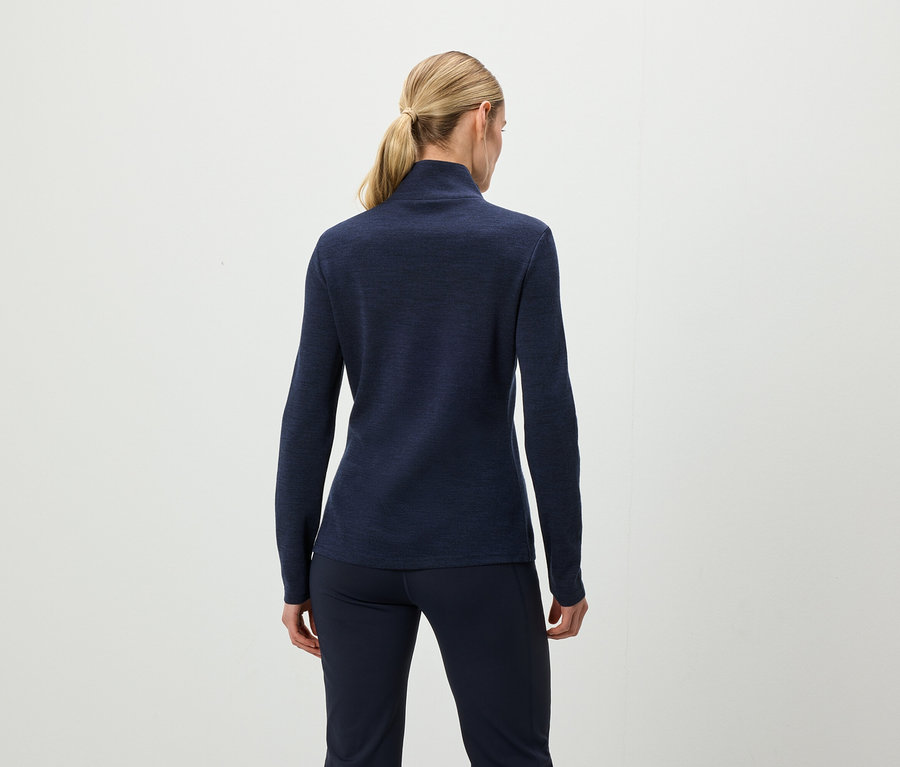 Vue de dos, une femme aux cheveux blonds attachés en queue de cheval porte un haut à manches longues bleu foncé et un pantalon bleu foncé.