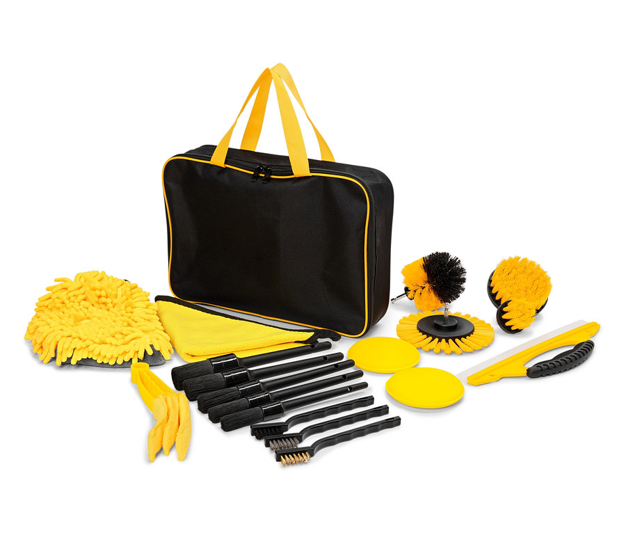 Un sac noir avec des poignées et une bordure jaunes entouré de gants de toilette, de serviettes, de brosses et d'éponges jaunes.