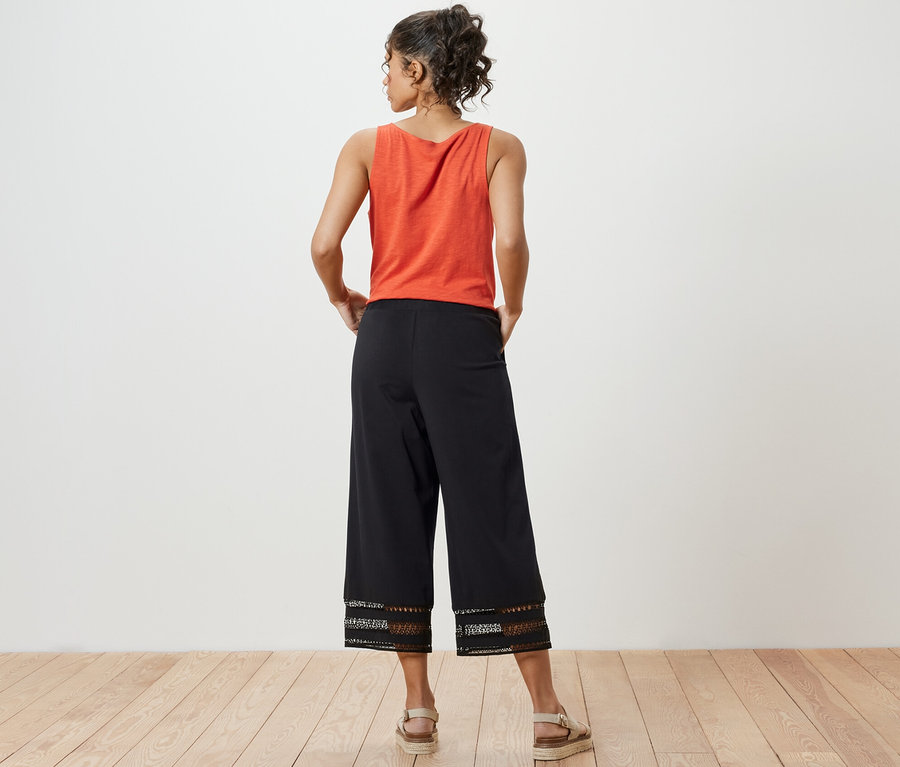 Une femme, vue de dos, porte un haut orange et un pantalon large noir à broderie.