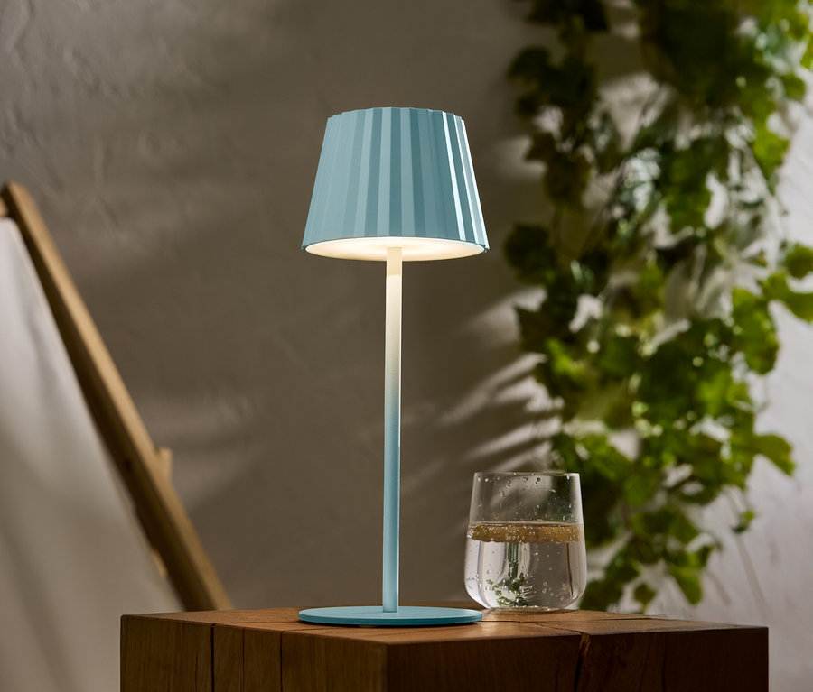 Une lampe bleue rayée est posée sur une table en bois, à côté d'un verre d'eau.