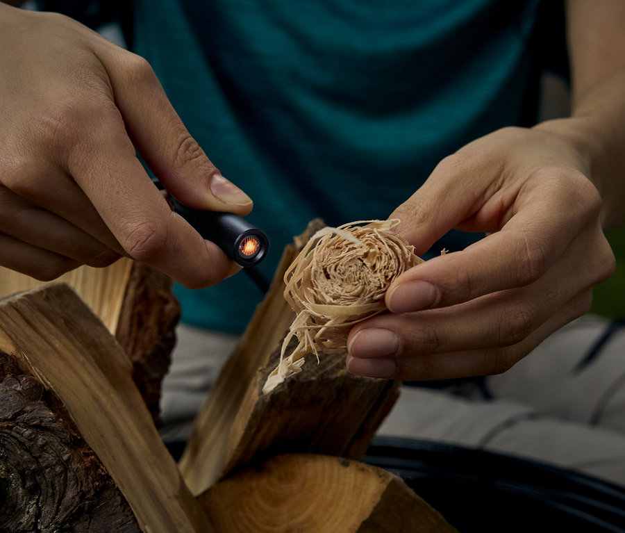 Une personne allume une allumette avec un briquet à tige, à côté de morceaux de bois.