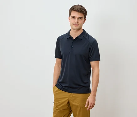 Homme portant un polo bleu marine et un pantalon marron doré, une main dans la poche.