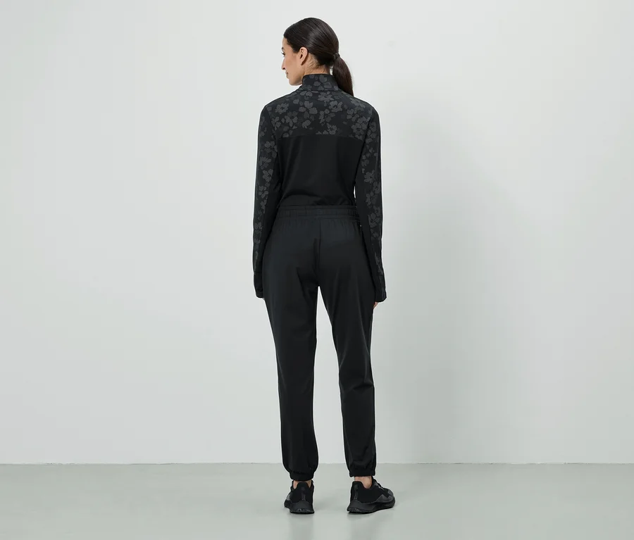 Femme vue de dos portant un survêtement noir avec motif floral sur les manches et les épaules, et des baskets noires.