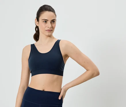 Femme avec queue de cheval portant un soutien-gorge de sport bleu marine et un legging, posant sa main sur sa hanche.