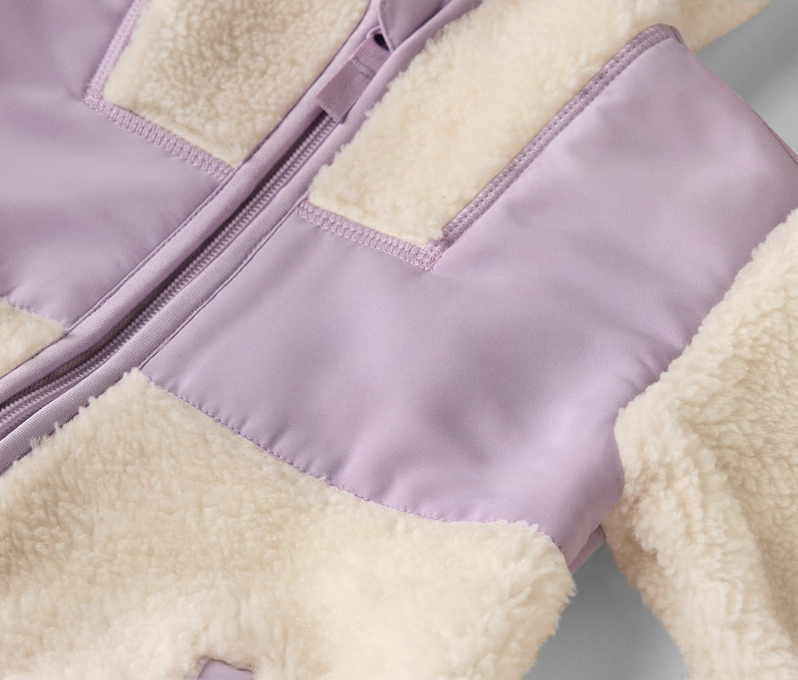 Gros plan d'une veste avec fermeture éclair et panneaux de tissu moelleux crème et lavande.