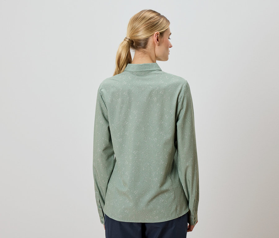 Une femme aux cheveux blonds porte une chemise vert clair à manches longues avec un motif à pois discret.
