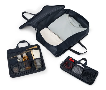 Trois sacs de voyage bleu marine ouverts avec des poignées et des fermetures éclair alignés sur un fond blanc. Les sacs contiennent des vêtements, des cosmétiques et des accessoires.