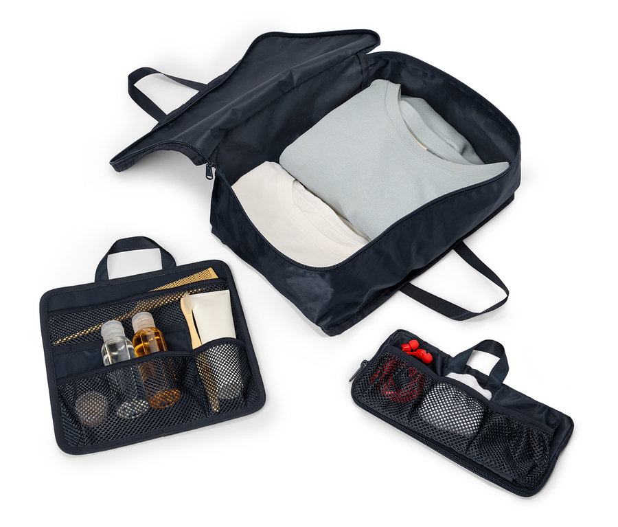 Trois sacs de voyage bleu marine ouverts avec des poignées et des fermetures éclair alignés sur un fond blanc. Les sacs contiennent des vêtements, des cosmétiques et des accessoires.
