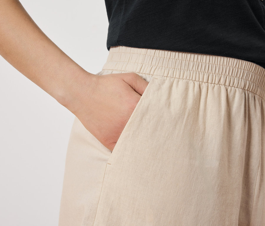 Femme avec la main dans la poche d'un pantalon beige.