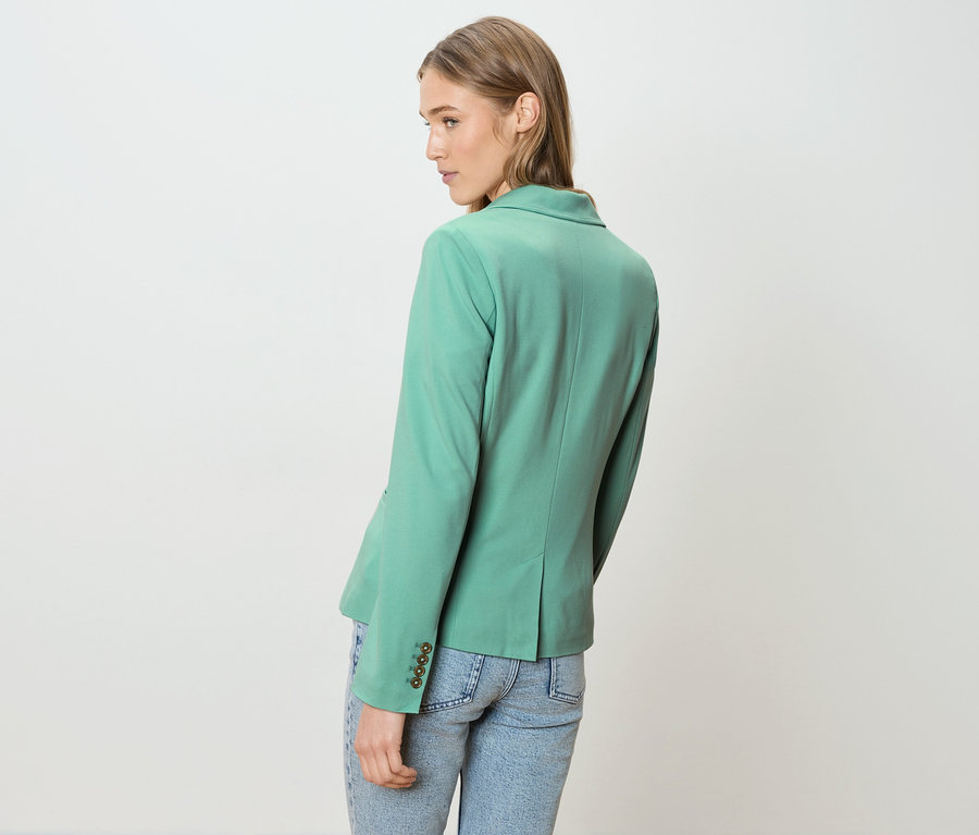 Femme vue de dos, portant un blazer vert et un jean.