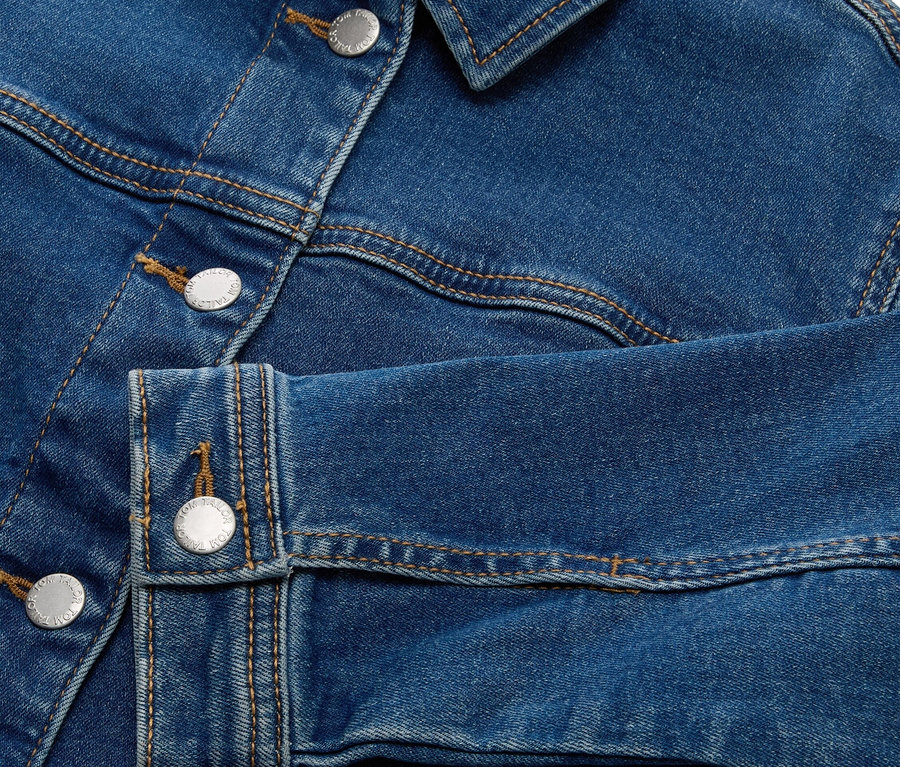 Gros plan sur une veste en jean bleue avec des boutons argentés.