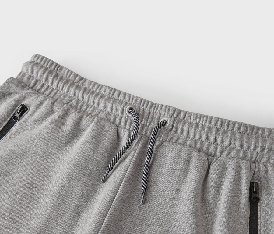 Gros plan de la taille d'un pantalon de survêtement gris avec cordon de serrage et poches zippées.