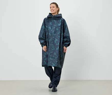 Une femme se tient debout dans un long poncho de pluie bleu à capuche avec un motif de feuilles.